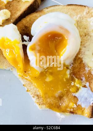 Runny poached egg on buttered white toast Stock Photo