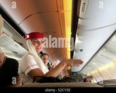 Emirates Airlines cabin crew assisting passengers in airplane before takeoff of aircraft Stock Photo