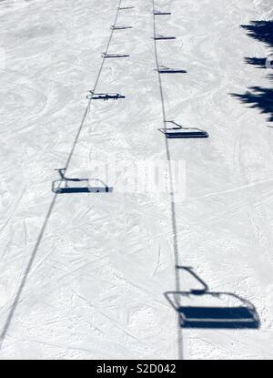 Shadows of the ski lift chairs in the snow on the bright sunny winter day. Stock Photo