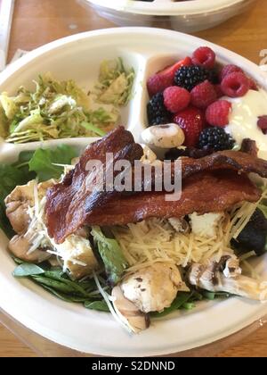 Mixed selection lunch buffet on recycled cardboard plate included bacon, mixed salad leaves, grated cheese, mushrooms, with side of Summer fruits including black and raspberries in plain Greek yogurt Stock Photo