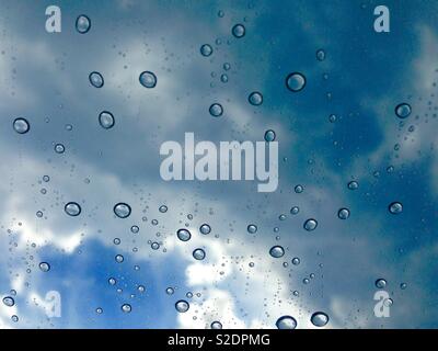Water droplets on window with clouds and sky in background Stock Photo