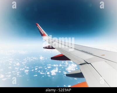 Easyjet airplane wing during flight over ocean with blue sky and cloud background Stock Photo