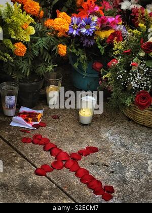 A cross made from red rose petals decorates a gravesite surrounded by fresh flowers honoring a loved one on Día de Los Muertos in Mexico. Stock Photo