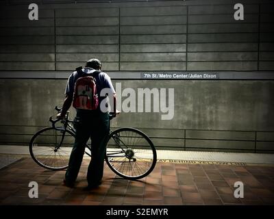 Man wearing pink backpack waits with bicycle for LA Metro train on platform at 7th Street Metro Center in Downtown Los Angeles Stock Photo