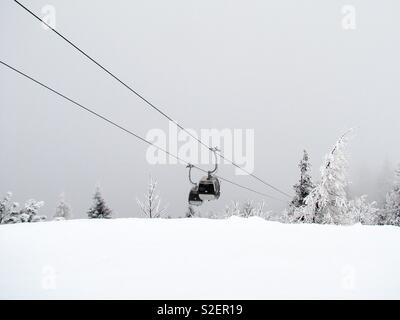 A ski cable car emerges from the fog above the snow-covered mountain top and meets the funicular cabin, which is on the way down into The Valley Stock Photo