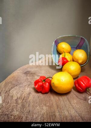 Healthy still life of lemons & red spicy peppers, on a wooden textured table. Stock Photo