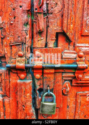 Rusty, padlocked door with peeling red paint symbolizes confinement and abandonment, evoking feelings of entrapment, neglect, and isolation Stock Photo