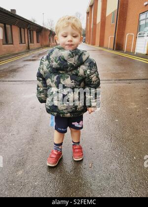 Two year old boy wearing his jacket the wrong way round. Hampshire, England, United Kingdom. Stock Photo
