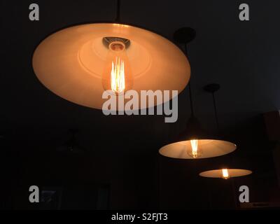 Three tungsten l-carbide incandescent filament lights with exposed glass bulbs in dark space Stock Photo