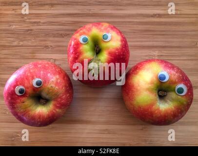 Creative healthy fun food concept. Three Pink Lady apples with googly eyes on a bamboo board with copy space Stock Photo