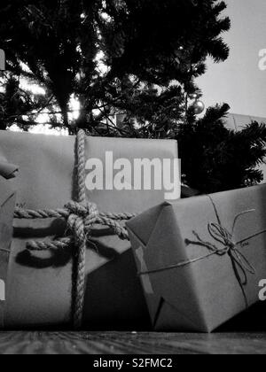 Crisp black and white photo of paper wrapped gifts under the Christmas tree tied with string and rope Stock Photo