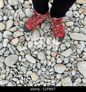 Person wearing hiking boots on pebbled beach Stock Photo