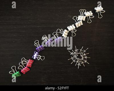 Paper fasteners and push pins arranged in pattern on dark wood desk Stock Photo