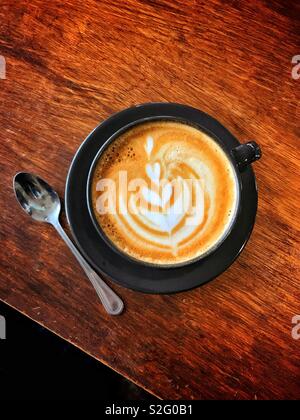 An overhead image of a cup of Latte Coffee. Spoon is on the wooden table. There is space for copy or text either at the top or bottom of the photo area. Stock Photo