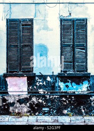 Broken wooden shutters with peeling paint on windows and wall below Stock Photo
