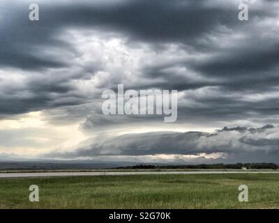 A shelf cloud hangs low over a foothills landscape with ominous clouds above. Stock Photo