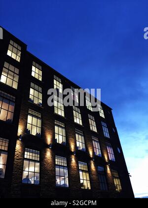 The exterior of a modern office block at night with the glow of window light in the rows of windows lighting up the interior rooms Stock Photo