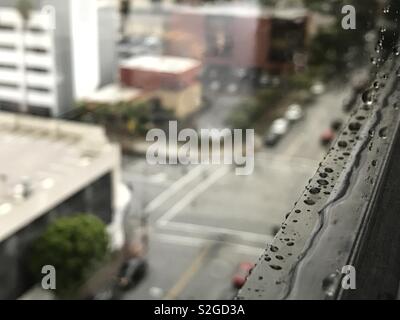 Raindrops on the window sill of a high rise building are shown during a rainy car. Stock Photo