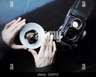 Man’s hands holding plate with chocolate treat on the table with film camera Stock Photo