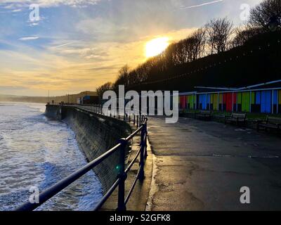 Filey seafront, at high tide on a winter’s afternoon showing a row of closed up beach huts Stock Photo