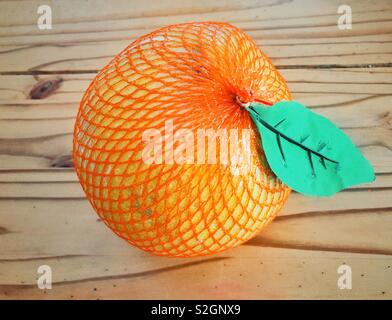 Pomelo fruit wrapped in mesh with fake leaf from grocery store on wooden table Stock Photo