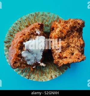 Closeup of homemade carrot muffin torn in half on wrapper with butter on one side against blue background Stock Photo