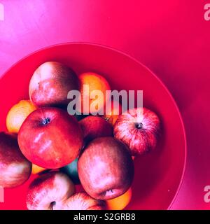 Red bowl with red apples and oranges on red table top view Stock Photo