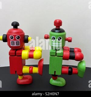 Two brightly coloured wooden toy robots balanced on one leg as if marching or dancing Stock Photo