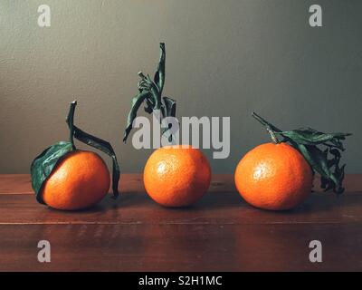 Three clementines with stems on a wooden surface with grey background Stock Photo