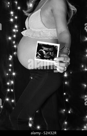 BW photo of a pregnant woman holding ultrasound scan of her baby. Stock Photo