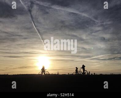 Cyclists are silhouetted against the setting sun as they wheel their bikes at Walthamstow Wetlands, London, UK. Stock Photo