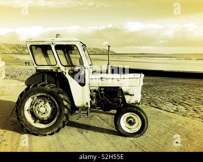 Old tractor parked on a slipway on the coast Stock Photo