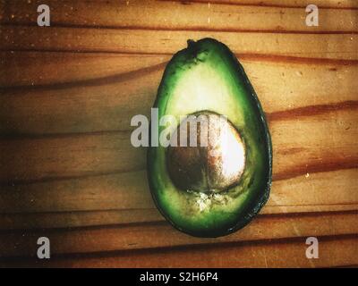 Rustic image of half an avocado with pit on wooden surface Stock Photo