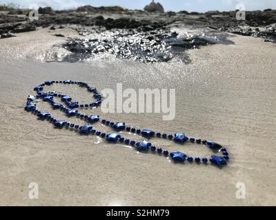 A necklace with blue stars lies on a beach. Stock Photo