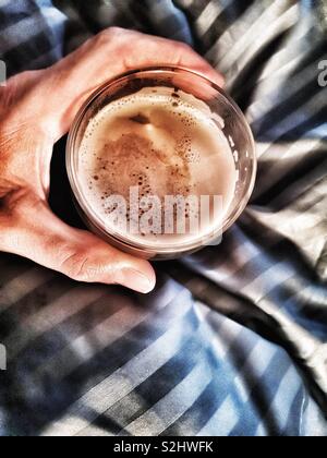 Top view of man’s hand holding glass of cafe latte in bed Stock Photo