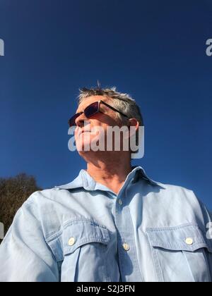 Man wearing sunglasses in a Chambray shirt against a deep blue sky. Stock Photo