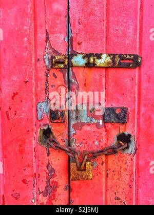 Old locks on an old garage door with peeling red paint. Stock Photo