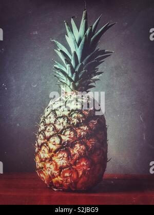 Pineapple on wooden surface with grey background Stock Photo