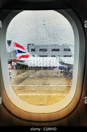 Raindrops on the window of a plane with another airliner blurred in the background Stock Photo