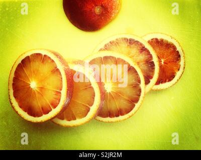 Blood orange cut into slices on lime green cutting board Stock Photo