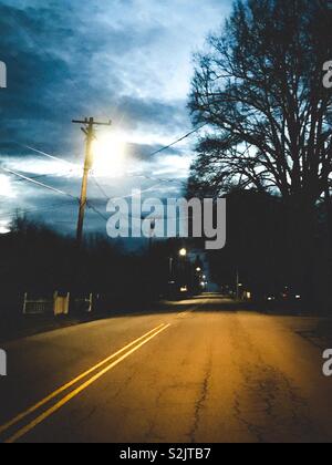 Dark before dawn on deserted street with trees in silhouette Stock Photo