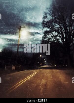 Grunge effect photo of the dark before dawn on deserted street with trees in silhouette and street lights Stock Photo