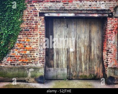 Old garage door set in a brick wall with ivy Stock Photo