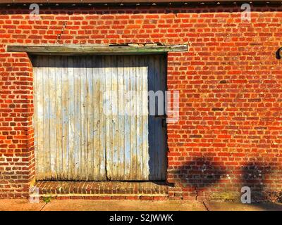 Garage door with flaking pale blue paint in a red brick wall. Stock Photo