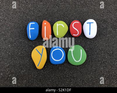First you, motivational message composed with multi colored sea stones over natural black volcanic sand Stock Photo