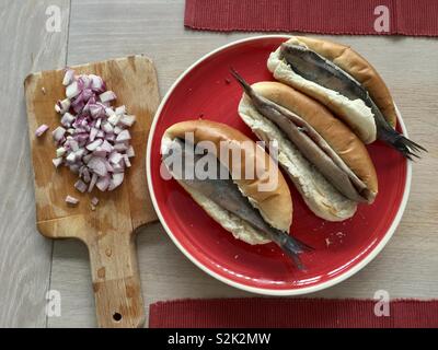 Traditional Dutch herring in bread with onions on a wooden table Stock Photo