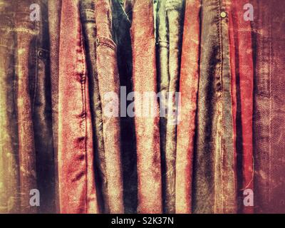 Side view of many fashionable red and orange hued jeans hanging on a clothing rack. Stock Photo