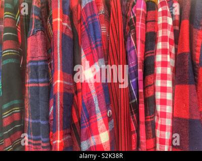 Side view of many fashionable red, blue, and black hued patterned and checkered clothes hanging on a clothing rack. Stock Photo