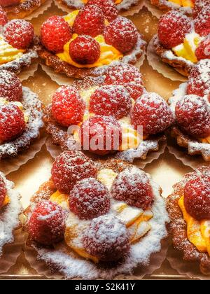 Fresh delicious and mouth watering professionally baked raspberry tarts with cream and powdered sugar. Stock Photo