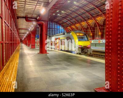 Antwerp central station in Antwerp, Belgium, as seen from the inside on the first or top platform with a train waiting on the rails at the platform, showing the structure of the old glass roof. Stock Photo